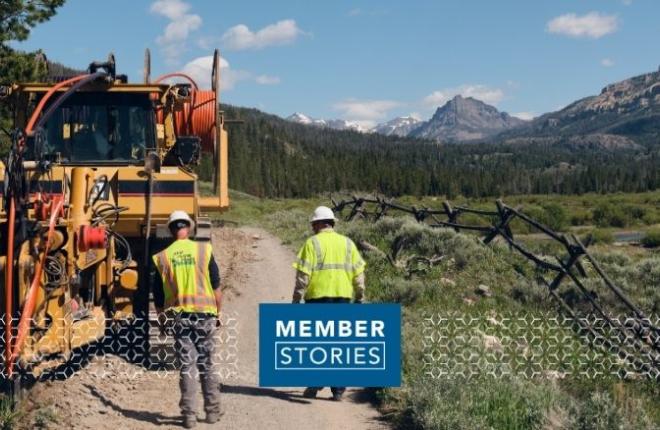 Hero image: two lineworkers walking on trail, back facing, yellow tractor on left side. Mountains in distance
